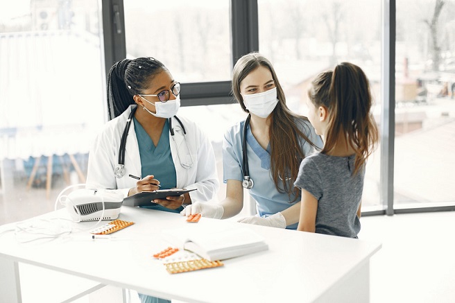 A female doctor and female nurse, both wearing a nose mask talking to a female child